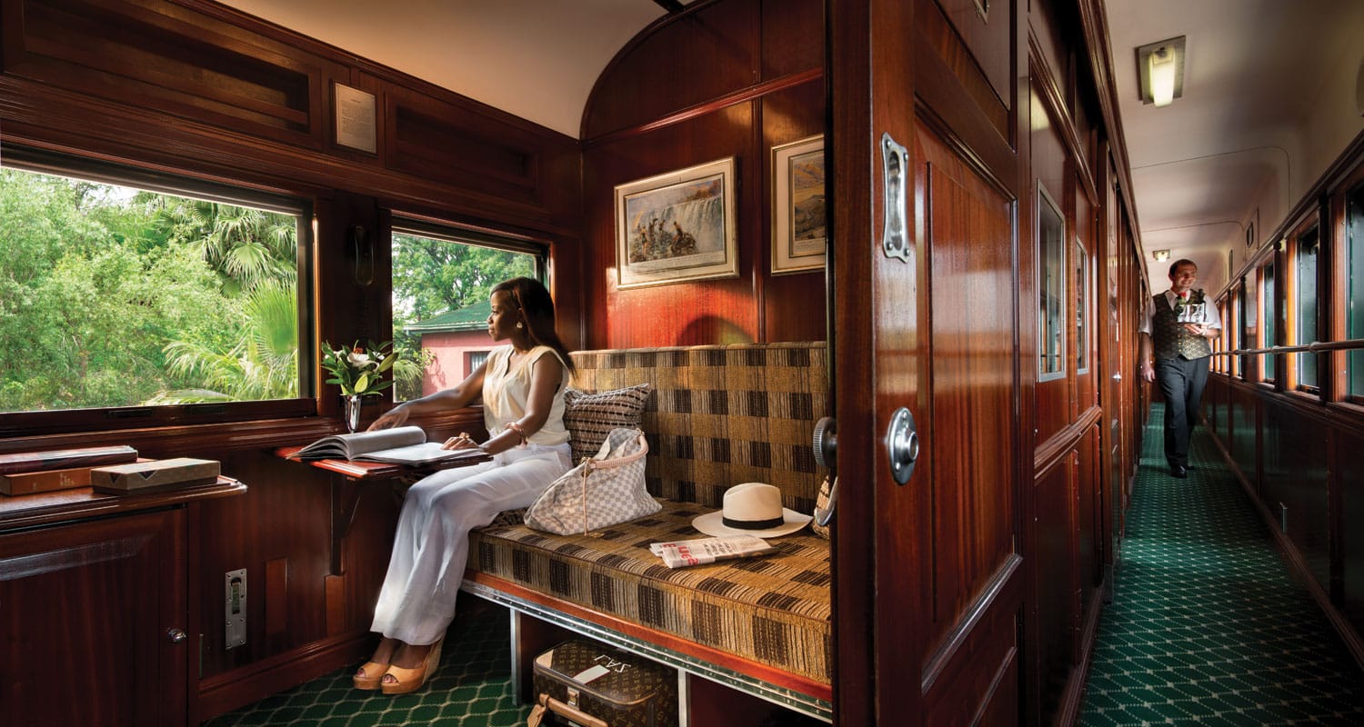 Voyage en train luxueux avec une ambiance élégante, offrant une vue sur la nature verdoyante. TMR Voyages.